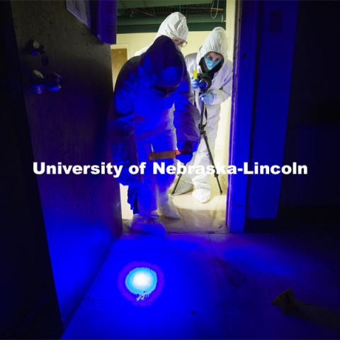 Symone Arends, a senior from Lincoln, shines an ultraviolet light onto the floor. The light will make body fluids and fibers glow when viewed through the orange filter she holds. Arends is working a mock crime scene in a basement room in Filley Hall. Forensic Science 485 is the capstone for the seniors. The CSI option students work a mock crime scene while the biochemistry option students process the samples. The class concludes with a mock trial. March 2, 2021. Photo by Craig Chandler / University Communication.