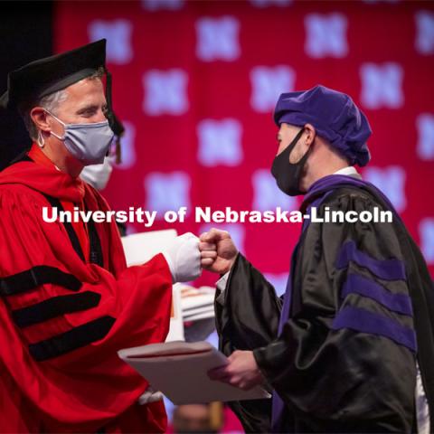 Adam Podraza receives a fist bump from Dean Richard Moberly after receiving his hood. College of Law Graduation at Pinnacle Bank Arena. May 7, 2021. Photo by Craig Chandler / University Communication.