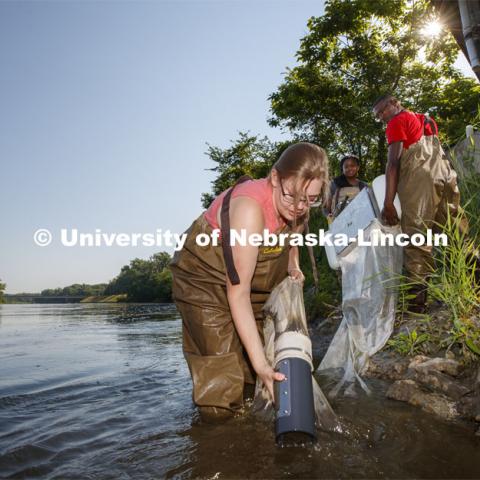 Meredith Sutton, graduate student in environmental engineering, pulls the sediment collection jar out of the Elkhorn River as she, McNair scholar Seth Caines and summer research scholar Moriah Brown from Howard University use a floating sieve to sample water in the Elkhorn River. They are working with Professor Shannon Bartlet-Hunt researching textiles as a source of microplastic fibers to Nebraska streams. July 2, 2021. Photo by Craig Chandler / University Communication.