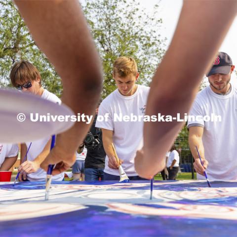 Riley Berner, a senior from Norfolk, is framed by fellow painters working on “Lift Off”. Lift Off is an entrepreneurial community mural painting in the green space outside the Nebraska Union. The student-created design will be hung in the College of Business. September 1, 2021. Photo by Craig Chandler / University Communication.