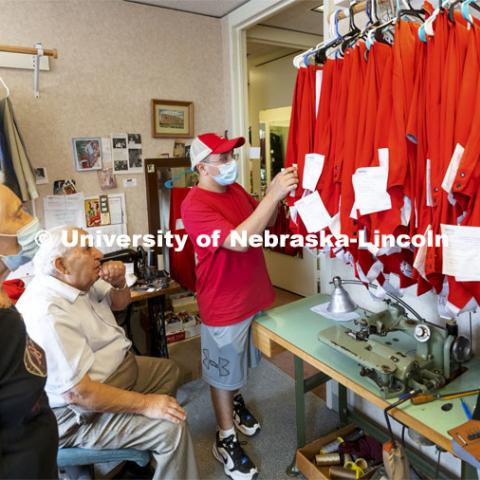 Demetrios Deligiannis and his wife Stamatia watch as Alfonso Meza picks up his altered uniform pants in preparation for the first home game this Saturday. This year, each member of the band received new pants for the season. Each of the 300 pairs was custom tailored by the couple. Demetrios and Stamatia Deligiannis have been altering the Cornhusker Marching Band uniforms for 50 years from their Lincoln tailoring business. September 1, 2021. Photo by Craig Chandler / University Communication.