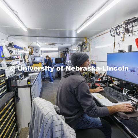 Jim Holloway and Karla Lechtenberg work on the computer connections and camera views in a trailer rigged to record the information at the crash test site. Researchers from the Midwest Roadside Safety Facility conducted a rare tractor-tanker crash to test how a newly designed and significantly less tall concrete roadside barrier performs in a crash. The test was at the facility’s Outdoor Proving Grounds on the western edge of the Lincoln Municipal Airport. December 8, 2021. Photo by Craig Chandler / University Communication.