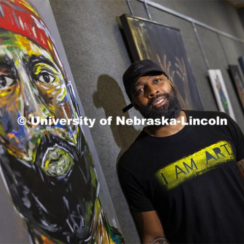 Jevon Woods poses next to a self-portrait entitled “Jevon”. Woods is a Black artist from Lincoln whose work is on display in the loft gallery at the East Campus Union through this month as part of Black History Month. February 9, 2022. Photo by Craig Chandler / University Communication.
