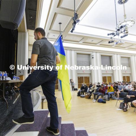 Mykhailo Smyshliaiev, a member of the Ukrainian community in Lincoln carries the Ukrainian flag to the stage before he spoke. Stand With Ukraine! panel discussion in the Nebraska Union ballroom Tuesday afternoon. March 1, 2022. Photo by Craig Chandler / University Communication.