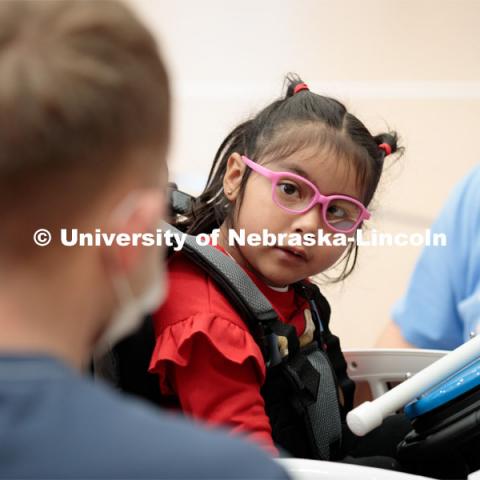 Four-year-old Dayana Torres looks at UNL engineering student Ethan Bowles, left, while being strapped into the new, battery-powered car that Bowles and his team modified for her.

Twice yearly, Nebraska’s Go Baby Go chapter modifies kid-sized battery powered cars for children with movement difficulties, providing them at no cost to the families. Nebraska’s GoBabyGo! chapter is funded by the Munroe-Meyer Guild. The program is a partnership between MMI's Department of Physical Therapy, the University of Nebraska-Lincoln and the University of Nebraska-Omaha Engineering Department and the UNMC College of Allied Health Professions/Physical Therapy students. The event took place on at the MMI building at 69th and Pine Streets in Omaha on Saturday, April 2, 2022. Photo by Kent Sievers / University of Nebraska Medicine.

