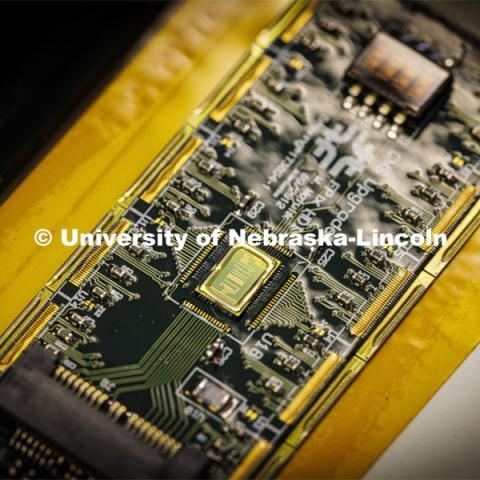Close up of a circuit being assembled for the Large Hadron Collider in Jorgensen Hall. Nebraska’s Caleb Fangmeier, a farm kid from Hebron, stayed up until 2 a.m. as an undergraduate to hear the announcement about the discovery of the Higgs boson. He now holds a doctorate in physics and works as a detector lab manager in Jorgensen Hall. His group is building nearly 2,500 particle detectors that will be used when the Large Hadron Collider restarts sometime between 2024 and 2026. In addition to Caleb, there is one postdoc, three graduate students and five undergraduates who work in the lab. They use gantrys to glue these things together with great precision. April 18, 2022. Photo by Craig Chandler / University Communication.