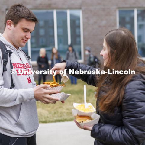 Jolie Peal grabs a fry from Brandon Mueting’s Motorfood lunch. Students lined up for Food Trucks @ Lunch. Students could use their meal plan for a lunch outside the Cather Dining Center. Food provided by: 

• MARY ELLEN’S …Food for the soul.

• MOTORFOOD …Lincoln’s hardest rocking food truck!

• SAY CHEESE …Amazing grilled cheese sandwiches on fresh, homemade bread. April 19, 2022. Photo by Craig Chandler / University Communication.