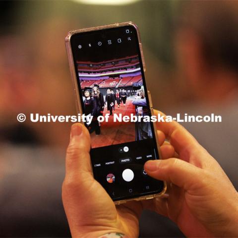 A family member snaps a photo on their phone of their grad marching in for commencement. Graduate commencement in Pinnacle Bank Arena. May 13, 2022. Photo by Craig Chandler / University Communication.