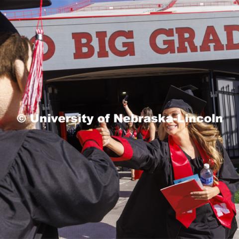 A graduate is greeted by Herbie Husker with a fist-bump. UNL undergraduate commencement in Memorial Stadium. May 14, 2022. Photo by Craig Chandler / University Communication.