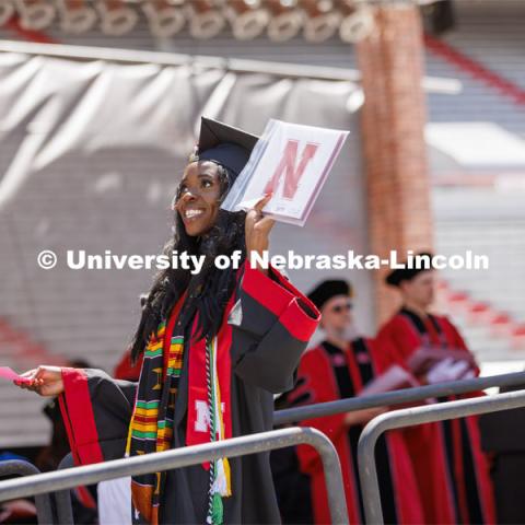 Chika Izuegbunam holds her diploma up as she walks off the stage so the cameras can show her on the video screen in Memorial Stadium. UNL undergraduate commencement in Memorial Stadium. May 14, 2022. Photo by Craig Chandler / University Communication.