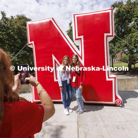 Grace and Emma Alder, twin sisters from Atkinson, NE, pose for NSE Leader Hannah-Kate Kinney in front of an inflatable N sculpture on the Union Plaza. New Student Enrollment. June 1, 2022. Photo by Craig Chandler / University Communication.