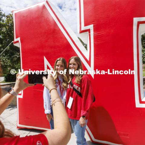 Grace and Emma Alder, twin sisters from Atkinson, NE, pose for NSE Leader Hannah-Kate Kinney in front of an inflatable N sculpture on the Union Plaza. New Student Enrollment. June 1, 2022. Photo by Craig Chandler / University Communication.