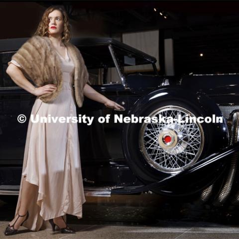 Anna Kuhlman evokes Hollywood glamour in a ’30s-style gown, featuring bias-cut panels and flowing sleeves in a soft pink. Paired with a vintage fur stole and T-strap heels, she poses next to a 1930 Duesenberg Model J at the Speedway Motors Museum of Speed. Kuhlman, who earned her master’s degree in May, researched fashion of the 1930s. June 7, 2022. Photo by Craig Chandler / University Communication.