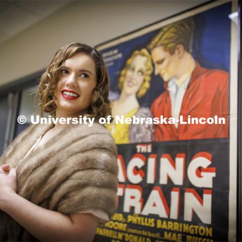 Anna Kuhlman poses in front of a poster for Racing Strain, a 1932 racing movie. Kuhlman, who earned her master’s degree in May, researched fashion of the 1930s. June 7, 2022. Photo by Craig Chandler / University Communication.