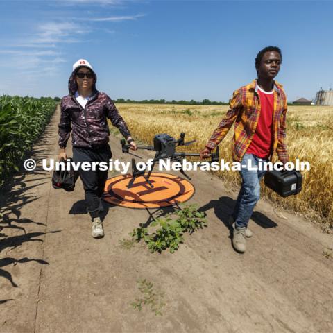 Biquan Zhao, PhD student in Biological Systems Engineering, and Pascal Izere, master’s student in Biological Systems Engineering, carry an autonomous drone back to the truck. The drone has been photographing a field of triticale at the research fields at 84th and Havelock. Biological Systems Engineering fieldwork with drones for phenotyping fields. June 27, 2022. Photo by Craig Chandler / University Communication.