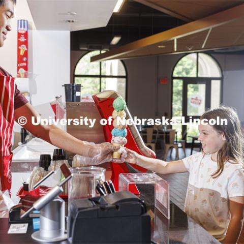 Randy Nguyen serves up a cone of colorful ice cream to Allie Wiesman, 9. She and her parents are visiting from Kentucky. Ice cream is scooped up at the Dairy Store on East Campus. July 18, 2022. Photo by Craig Chandler / University Communication.