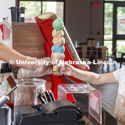 Randy Nguyen serves up a cone of colorful ice cream to Allie Wiesman, 9. She and her parents are visiting from Kentucky. Ice cream is scooped up at the Dairy Store on East Campus. July 18, 2022. Photo by Craig Chandler / University Communication.