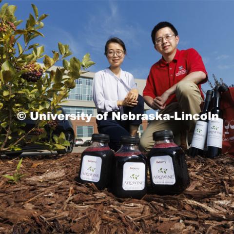 Xiaoqing Xie, left, and Changmou Xu pose with an Aronia berry bush growing outside of Food Innovation Center along with bottles of AroJuice and AroWine, a product by the A+ Berry Company. The goal of the Aronia berry research group is to convert Aronia berries, a superfruit mainly grown in the Midwest, into functional foods and ingredients. August 2, 2022. Photo by Craig Chandler / University Communication.