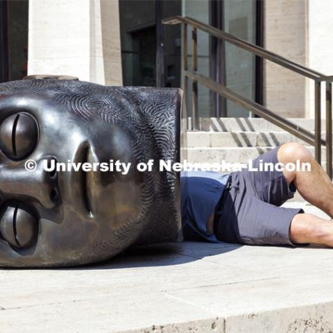 Big head, little body. Rob Jensen of Jensen Conservation of Omaha lays behind the Fallen Dreamer sculpture outside the Sheldon as he applies a coat of wax to the sculpture. September 15, 2022. Photo by Craig Chandler / University Communication.