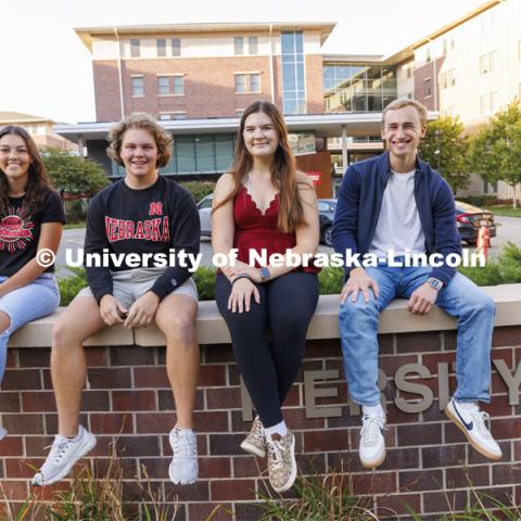 Students seated on a brick wall outside of University Suites Residence Hall. Housing Photo Shoot in University Suites Residence Hall. September 27, 2022. Photo by Craig Chandler / University Communication.