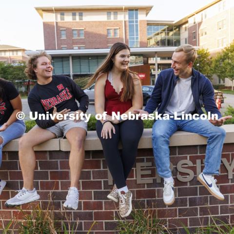 Students seated on a brick wall outside of University Suites Residence Hall. Housing Photo Shoot in University Suites Residence Hall. September 27, 2022. Photo by Craig Chandler / University Communication.