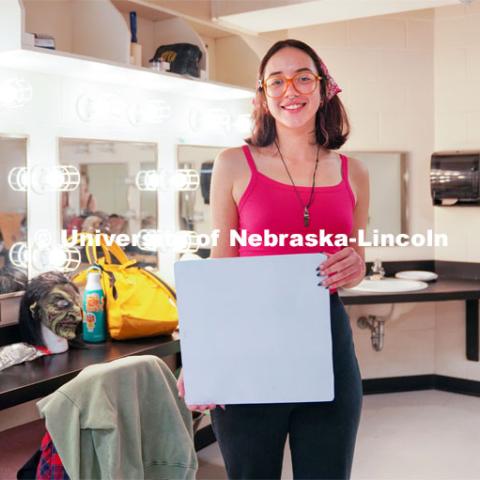 Standing in the dressing room of the Temple Building, Aurora holds up a sign that reads "I'm a Husker & Performing Shakespeare Around the World". As a longtime horror fan and recent Shakespeare convert, senior theatre performance major Aurora Villarreal sees their opportunity to play Lady Macbeth in UNL Repertory Theatre’s ShakesFEAR production as a particularly exciting — and unique — acting experience. October 12, 2022. Photo by Dillon Galloway for University Communication.