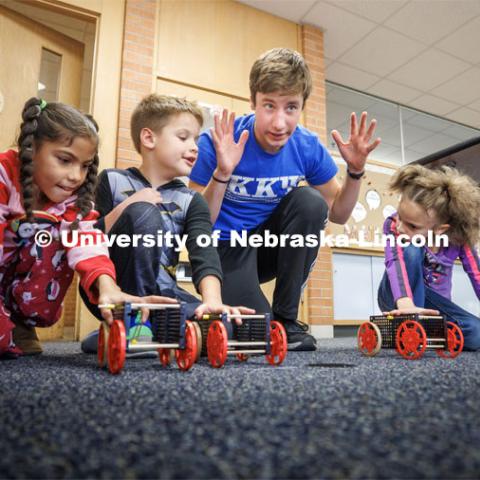 Spencer Knight gets three students and their rubber-band powered cars lined up for a race. Nebraska honors students Spencer Knight (blue shirt) and Rohan Tatineni (glasses) work with Riley Elementary students in their after-school STEM club. November 22, 2022. Photo by Craig Chandler / University Communication.