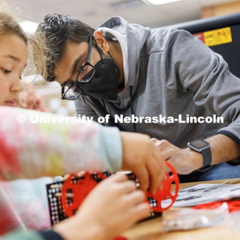 Rohan Tatineni helps a student build her rubber-band powered car. Nebraska honors students Spencer Knight (blue shirt) and Rohan Tatineni (glasses) work with Riley Elementary students in their after-school STEM club. November 22, 2022. Photo by Craig Chandler / University Communication.