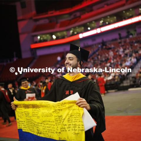 Juan David Jimenez Pardo waves the Colombian flag he carried through commencement. Pardo received his doctorate researching plant breeding and genetics. Graduate Commencement in Pinnacle Bank Arena. December 16, 2022. Photo by Craig Chandler / University Communication.