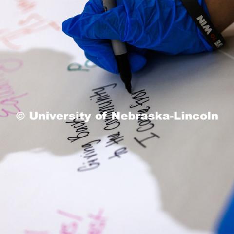 Mona Miller, a sophomore from Omaha, writes on a poster at the event. Volunteers assemble hunger kits filled with oatmeal. The goal was more than 2,000 kits. MLK Week. January 25, 2023. Photo by Craig Chandler / University Communication.
