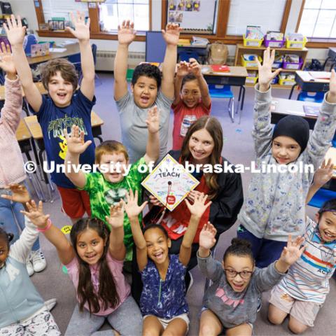 Morgan Twiss, dressed in her graduation gown and holding her mortar board, poses with the second-graders at Elliott Elementary, where she student-taught this spring. Twiss, a senior in elementary education from Central City will join Elliott full time as a second-grade teacher in the fall. April 13, 2023. Photo by Craig Chandler / University Communication.