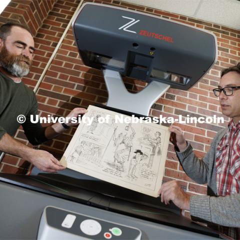 Richard Graham (right), Associate Professor in University Libraries, and John Wiese place an Oz Black cartoon onto the scanner bed to digitize the drawing. Graham and Wiese are building an online archive of editorial cartoons from Nebraska alumnus Oz Black. These cartoons are mostly from the 1920s and 1930s and ran in Nebraska newspapers headquartered in Lincoln. April 20, 2023. Photo by Craig Chandler / University Communication.