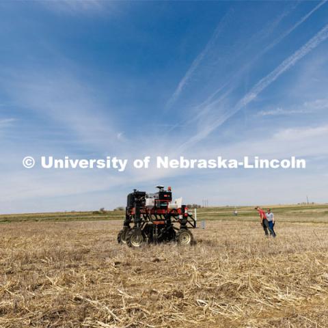 Graduate student Ian Tempelmeyer, red shirt, and graduate research assistant Taylor Cross walk behind the Flex-Ro autonomous planting robot as it starts a row. The self-driving robotic planter based on Santosh Pitla’s tractor platform works its way through a field at the Rogers Memorial Farm east of Lincoln. April 27, 2023. Photo by Craig Chandler / University Communication.