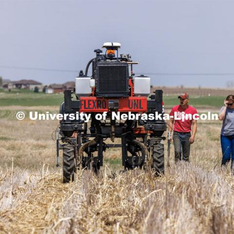 Graduate student Ian Tempelmeyer, red shirt, and graduate research assistant Taylor Cross walk behind the Flex-Ro autonomous planting robot as it starts a row. The self-driving robotic planter based on Santosh Pitla’s tractor platform works its way through a field at the Rogers Memorial Farm east of Lincoln. April 27, 2023. Photo by Craig Chandler / University Communication.