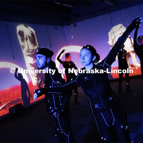 Isaiah Griffith and Marley Hewitt, second-year students in the Carson Emerging Media Arts program, pose in Mo-Cap (motion capture) suits with a group of students being filmed.  The suits with their infrared sensors (round dots vecroed to the suit) allow a ring of cameras to turn their motion into animated characters on screen. Students work in the Carson EMA MoCap (motion capture) lab. May 17, 2023. Photo by Craig Chandler / University Communication. 