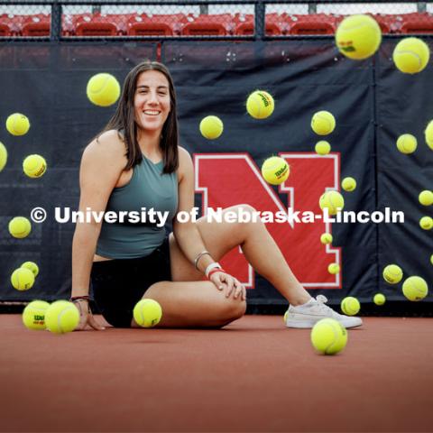 Tennis balls bounce around Isabel Adrover Gallego as she poses for a photo on the tennis court. Gallego, a senior in computer engineering and a Husker tennis player from Mallorca, Spain. Photo for Pride Month profile. May 18, 2023. Photo by Craig Chandler / University Communication.