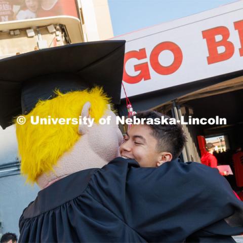 Husker Cheer Squad member Logan Larsen gets a hug from Herbie Husker before the ceremony. Undergraduate commencement at Memorial Stadium. May 20, 2023. Photo by Craig Chandler / University Communication.