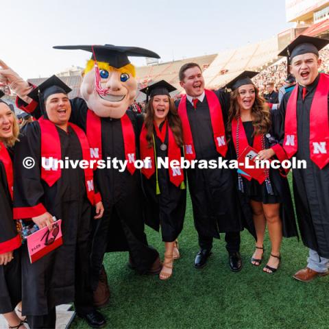A group of grads pose with Herbie for a photo. Undergraduate commencement at Memorial Stadium. May 20, 2023. Photo by Craig Chandler / University Communication.