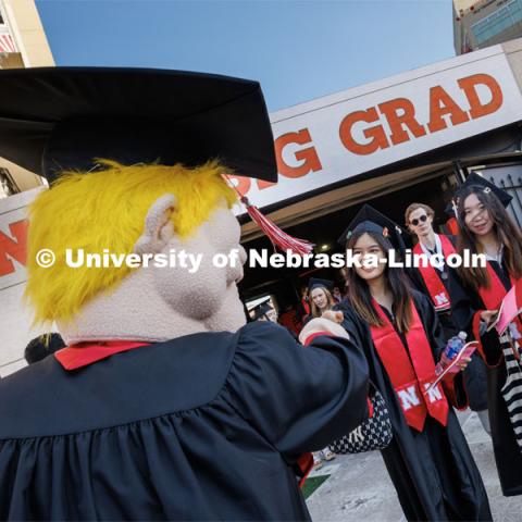 Herbie offers up a fist bump to grads as they enter the field. Undergraduate commencement at Memorial Stadium. May 20, 2023. Photo by Craig Chandler / University Communication.