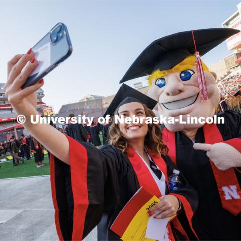 Sophia Frappier takes a selfie with Herbie Husker before the ceremony. Undergraduate commencement at Memorial Stadium. May 20, 2023. Photo by Craig Chandler / University Communication.
