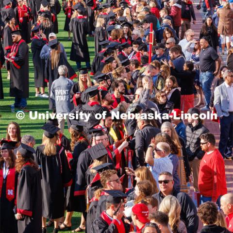 Graduates, friends and family meet before commencement begins at the red fence separating the field and the stands. Undergraduate commencement at Memorial Stadium. May 20, 2023. Photo by Craig Chandler / University Communication.