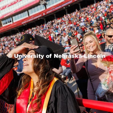 Angelique Fuentes squints into the sun as she tips her head back so her mother can photograph her decorated mortar board. Undergraduate commencement at Memorial Stadium. May 20, 2023. Photo by Craig Chandler / University Communication.