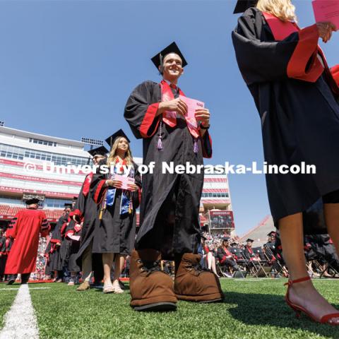Brendan Kauth-Fisher, a graduate in business administration, waits in line to receive his diploma. Brendan has been seen by thousands the past three years performing as Herbie Husker. Herbies are allowed to reveal themselves at commencement by wearing Herbie’s shoes to walk. Undergraduate commencement at Memorial Stadium. May 20, 2023. Photo by Craig Chandler / University Communication.