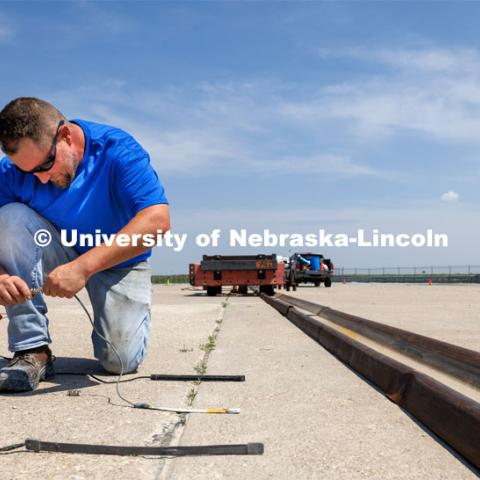 Christopher Charroin connects monitor cables that will be used to record data from a test of a sled will be pulled at a high speed. How the sled stops will test the strength of a ground anchor which will stop the moving sled. Cody Stolle, Research Assistant Professor and Assistant Director of the Midwest Roadside Safety Facility is leading a group researching better checkpoint barriers to help the Department of Defense. June 5, 2023. Photo by Craig Chandler / University Communication.