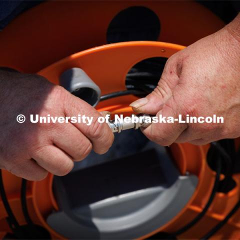 Christopher Charroin connects monitor cables that will be used to record data from a test of a sled will be pulled at a high speed. How the sled stops will test the strength of a ground anchor which will stop the moving sled. Cody Stolle, Research Assistant Professor and Assistant Director of the Midwest Roadside Safety Facility is leading a group researching better checkpoint barriers to help the Department of Defense. June 5, 2023. Photo by Craig Chandler / University Communication.