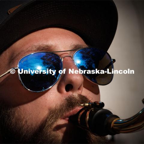 Sunset flares in the sunglasses of Christian Dahlman of Lincoln. The band practices on the greenspace by the Sheldon Art Museum as their normal pregame concert area next to the Kimball Recital Hall is under construction. Cornhusker Marching Band practice. August 16, 2023. Photo by Craig Chandler/ University Communication.