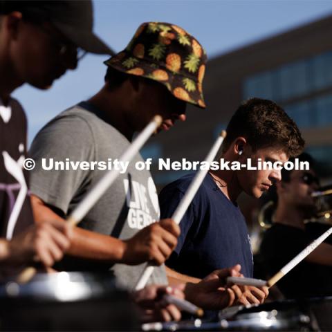 Sunset lights the face of Carston Swanson of Grand Forks, North Dakota, and fellow drumline members. The band practices on the greenspace by the Sheldon Art Museum as their normal pregame concert area next to the Kimball Recital Hall is under construction. Cornhusker Marching Band practice. August 16, 2023. Photo by Craig Chandler/ University Communication.