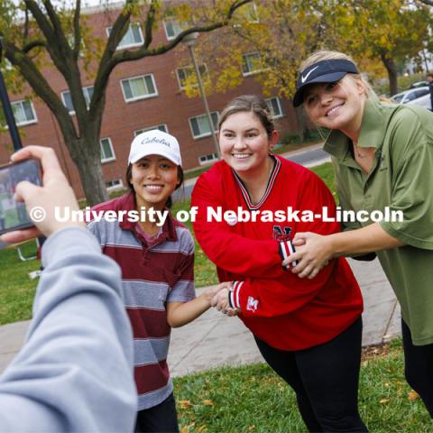 Nghi Ho, left, and Mackenzie Noble, right, have their photograph taken with Grace Puccio, tournament director and assistant director of alumni and student engagement. The handshake was for a successful participation. The two were competing for Alpha Xi Delta. Cornhole Tournament for Homecoming in the greenspace by the Nebraska Union. October 25, 2023. Photo by Craig Chandler / University Communication.
