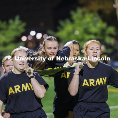 Army cadet Natalie Karrek rides the litter during the casualty evacuation race carried by, clockwise from front center, Rianna Wells, Michaela Guzman, Alyssa Batista and Grace Charlesworth. Cadet Remy Abdulahi shouts encouragement as the team races around the soccer field on Mabel Lee fields. Each branch ran a timed 220 yard race for the male and female cadets and midshipman. ROTC Joint Field Meet is like an ROTC Olympics for the Nebraska cadets and midshipman. Army, Air Force and Navy/Marine cadets compete in events such as Maneuvering Under Fire, Log Sit-ups, Tug-Of-War, Casualty Evacuation and Ultimate Frisbee. Army beat Navy in a sudden death 4x400 relay to claim the title. October 26, 2023. Photo by Craig Chandler / University Communication.