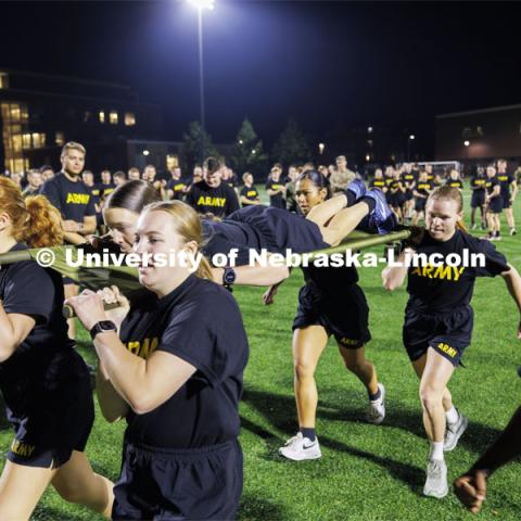 Army cadet Natalie Karrek rides the litter during the casualty evacuation race carried by, clockwise from front center, Rianna Wells, Michaela Guzman, Alyssa Batista and Grace Charlesworth. Cadet Remy Abdulahi shouts encouragement as the team races around the soccer field on Mabel Lee fields. Each branch ran a timed 220 yard race for the male and female cadets and midshipman. ROTC Joint Field Meet is like an ROTC Olympics for the Nebraska cadets and midshipman. Army, Air Force and Navy/Marine cadets compete in events such as Maneuvering Under Fire, Log Sit-ups, Tug-Of-War, Casualty Evacuation and Ultimate Frisbee. Army beat Navy in a sudden death 4x400 relay to claim the title. October 26, 2023. Photo by Craig Chandler / University Communication.